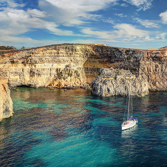 Segelboot vor den Felsklippen und dem türkisfarbenen Wasser der Lagune von Comino, Malta.