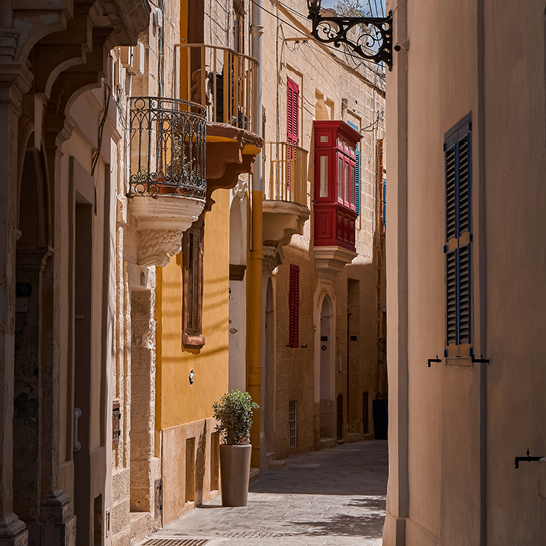 Schmale Gasse mit historischen Steingebäuden und farbigen Holzbalkonen in Rabat, Malta.