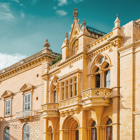 Historische Fassade aus hellem Stein mit verzierten Bögen und Balkon in Valletta, Malta.