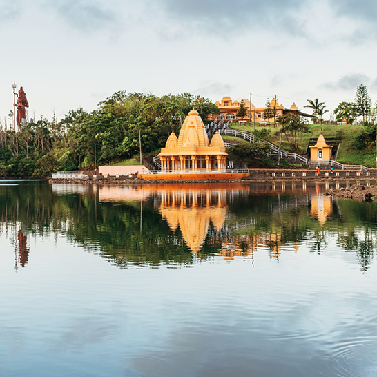 Ein Tempel spiegelt sich im Wasser neben einem Hügel in Mauritius wider.