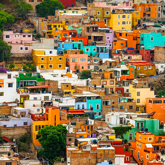 Bunte Häuser dicht an einem Hang in Guanajuato, deren kräftige Farben ein lebendiges Stadtbild formen.