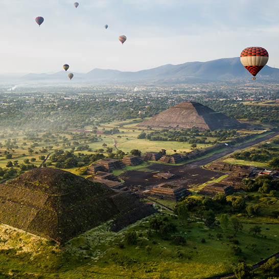 Luftaufnahme von Teotihuacán mit der Sonnen‑ und Mondpyramide sowie bunten Heißluftballons über der antiken Anlage.