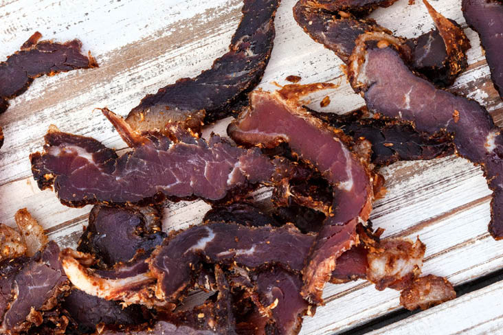 Getrocknete, gewürzte Fleischstreifen auf einer rustikalen weißen Holzoberfläche, unterschiedlich in Farbe und Textur.
