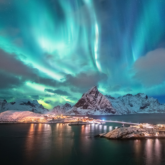Die Aurora-Lichter leuchten über einer Stadt und Bergen in Norwegen, umgeben von Licht und Schatten.