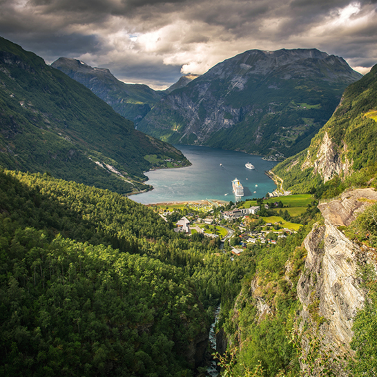 Blick auf die Bergkette von Geirangerfjord mit einem Fluss und einem Boot im Vordergrund.
