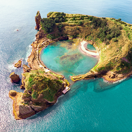 Vue aérienne d'une petite île avec une piscine bleue au centre, entourée d'eau turquoise.