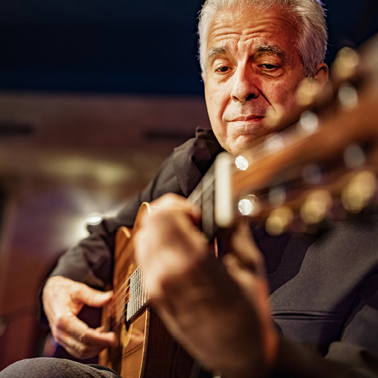 Un homme aux cheveux blancs en train de jouer de la guitare acoustique, concentré sur sa musique.