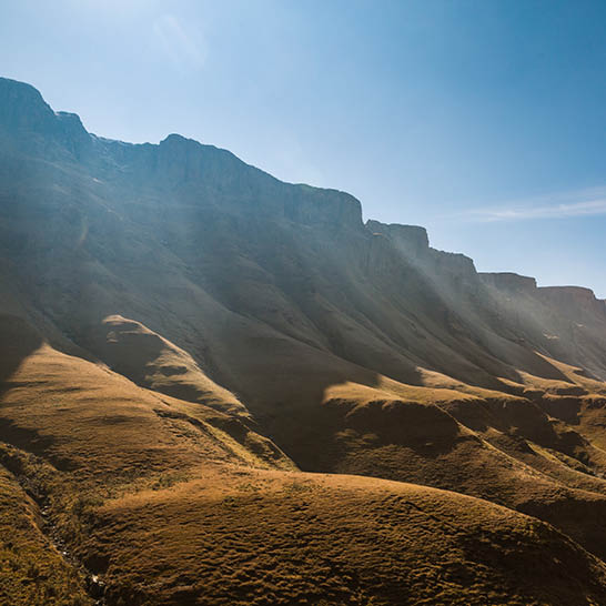 Berglandschaft entlang der Garden Route mit trockenen Grashügeln und steilen Felsklippen unter klarem Himmel.