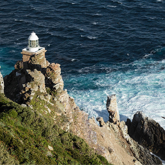 Leuchtturm am Kap der Guten Hoffnung auf felsiger Klippe über dem Meer.