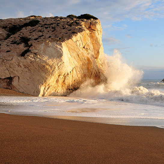 Aphrodite-Felsen an der Küste Zyperns, wo Wellen gegen die helle Felsformation am Sandstrand schlagen.