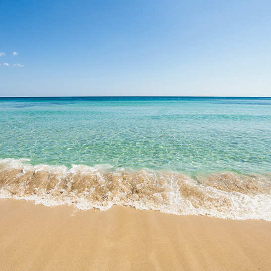Kristallklares Wasser, das sanft an den tropischen Strand von Gallipoli in Italien schwappt.