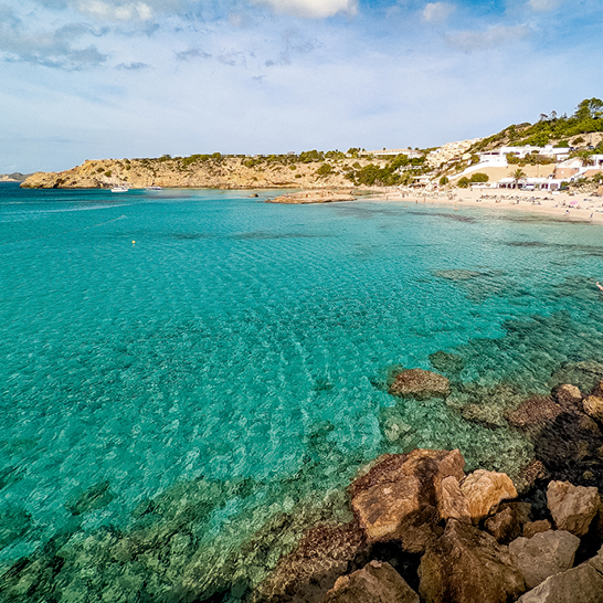 Strand von Cala Tarida in Ibiza, umgeben von Felsen und klarem Wasser.