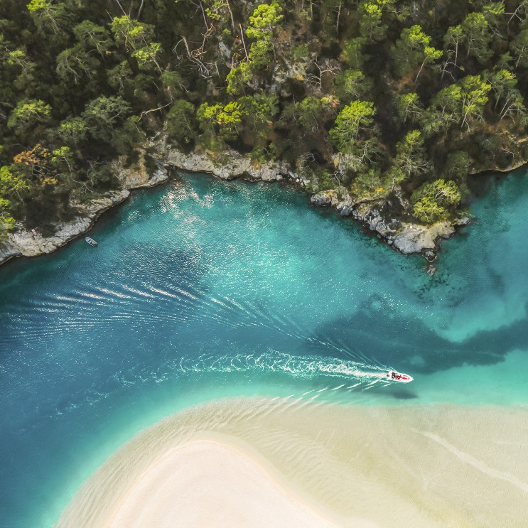 Luftperspektive einer blauen Bucht mit grüner Vegetation zur einen und weissem Strand zum anderen Ufer