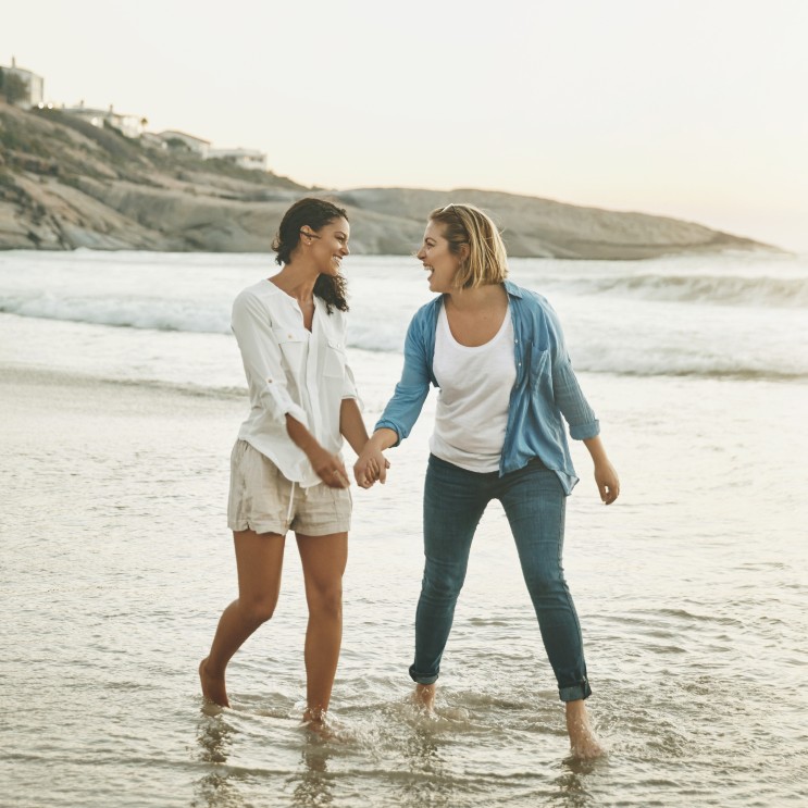 Zwei Frauen laufen Hand in Hand am Strand entlang